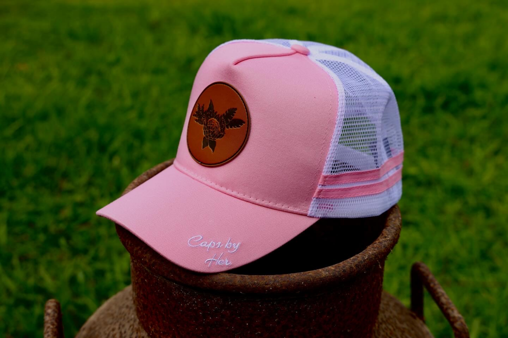 Baby pink Trucker cap with white mesh & SnapBack.
Leather patch on the front panel with a king Protea Flower.