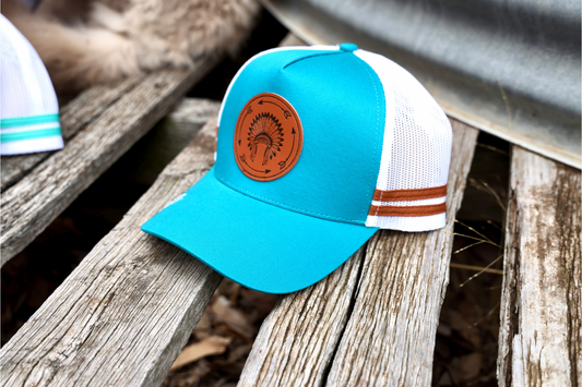 Teal blue Trucker cap with leather patch, Indian headdress + arrow.
Teal blue cap, under-brim cream Indian theme patterns. 
White mesh & snapback. 