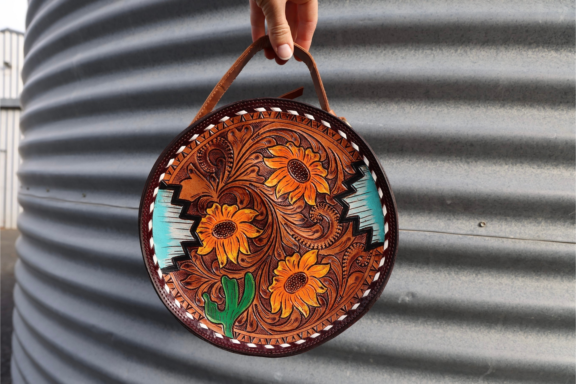 Round canteen bag featuring a hand tooled front panel, with a mix of floral, cactus & Aztec hand painted.